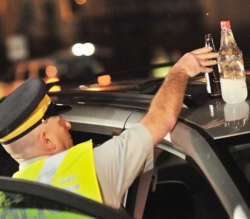 Police officer removes open liquor from a vehicle at a roadside check.