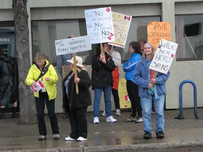 Protesters hold signs urging MP David Wilks to vote against the proposed budget bill at a rally in Cranbrook on Saturday (June 2).