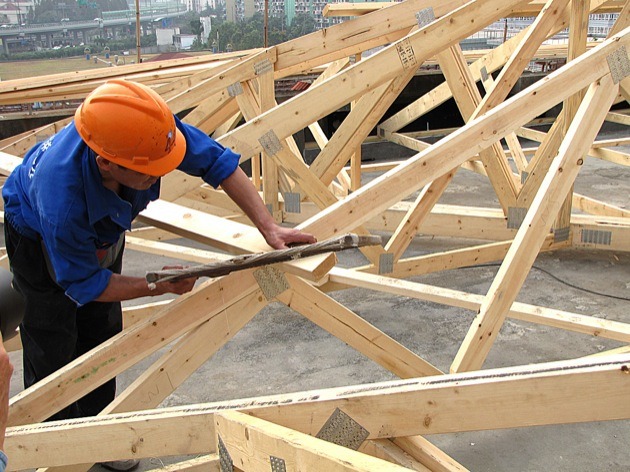 Chinese construction worker uses a hand saw to build wooden roof trusses on top of a concrete apartment building in 2009. Mass urbanization in China has created urgent new problems