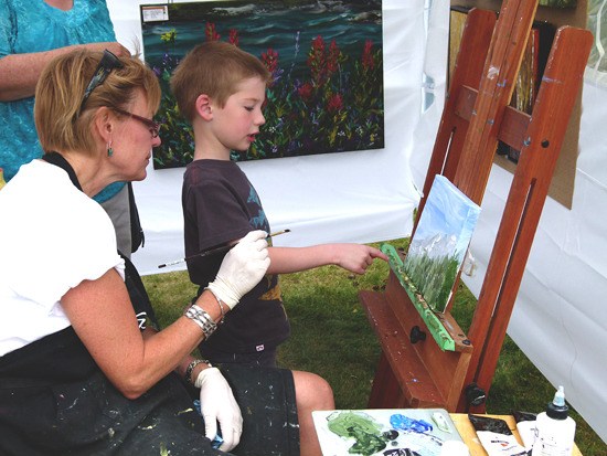 Artist Nancy Sorensen works on a landscape painting with a young boy.